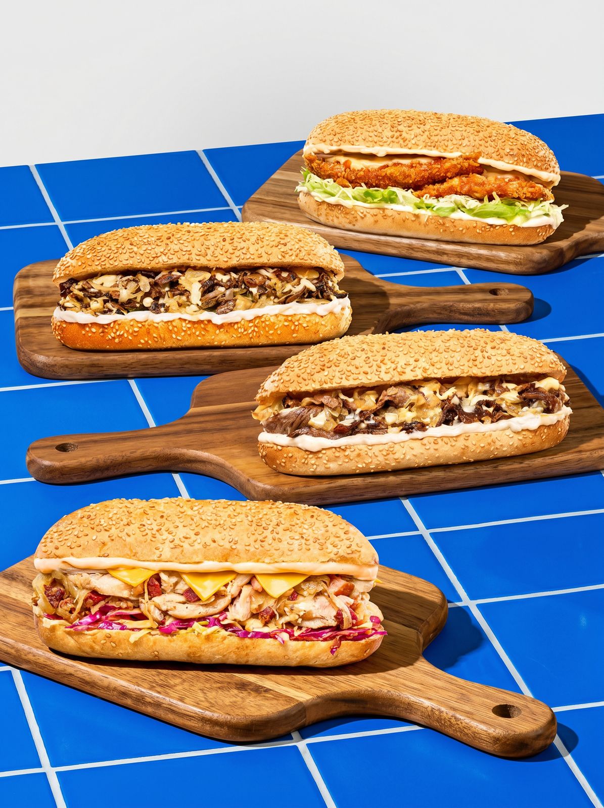 Cuatro sándwiches sobre tablas de madera y azulejos azules